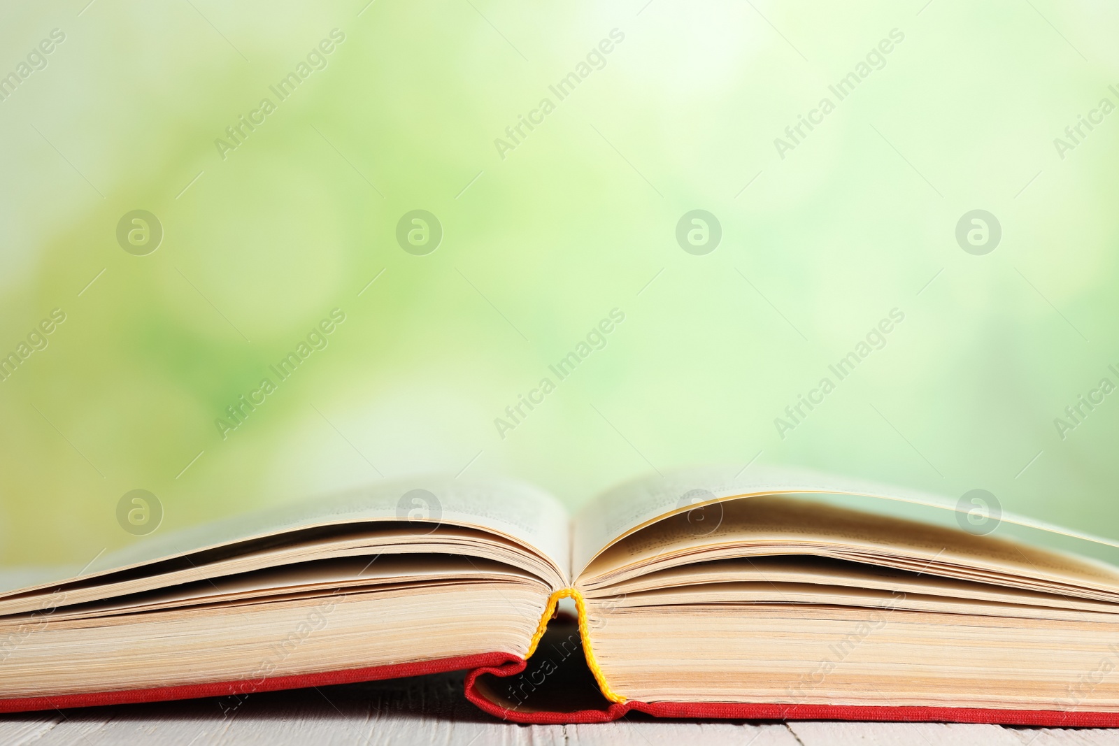 Photo of Open book on white wooden table against blurred green background, closeup. Space for text