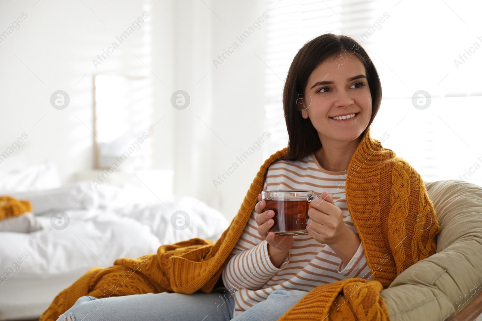 Photo of Woman covered with warm orange plaid enjoying hot drink at home
