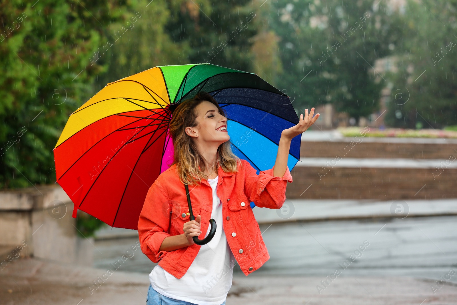 Photo of Happy young woman with bright umbrella under rain outdoors