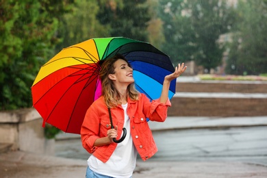 Happy young woman with bright umbrella under rain outdoors