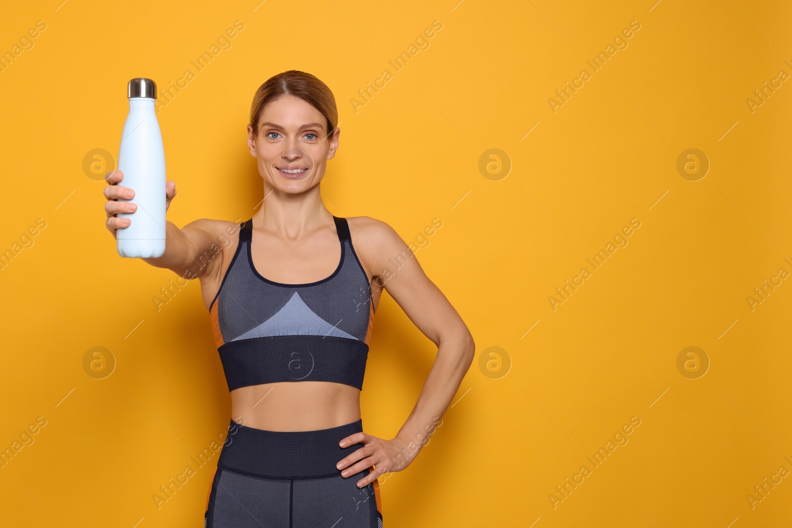 Photo of Sportswoman with thermo bottle on yellow background, space for text