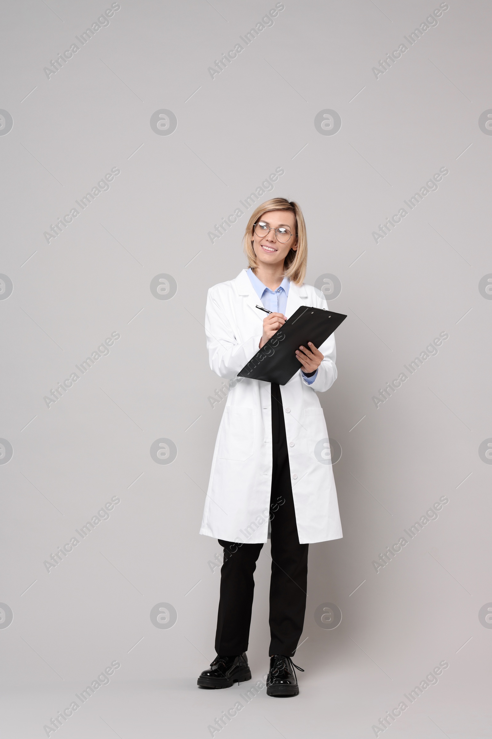 Photo of Smiling doctor with clipboard on grey background