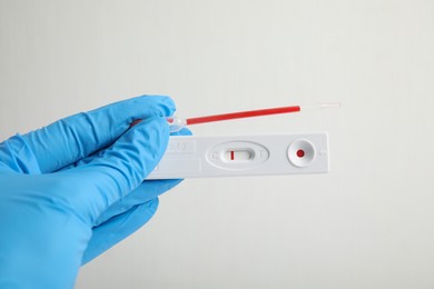 Photo of Doctor holding disposable express test for hepatitis and pipette with blood on white background, closeup