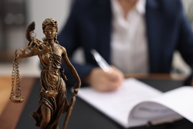 Notary signing document at table in office, focus on Lady Justice statue