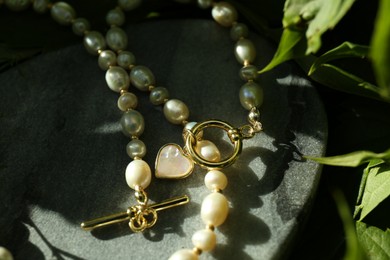 Photo of Stylish presentation of elegant pearl necklace on stone stand outdoors, closeup