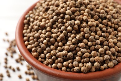 Dried coriander seeds in bowl on light table, closeup