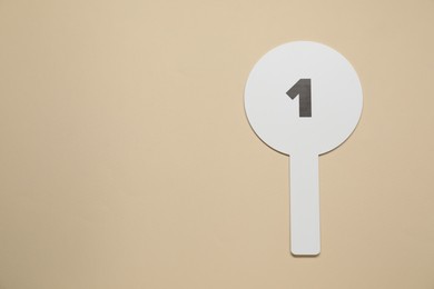 Auction paddle with number 1 on beige background, top view. Space for text