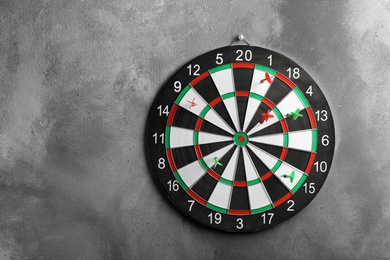 Photo of Arrows hitting dart board on grey wall. Space for text