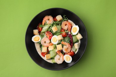 Photo of Delicious Caesar salad with shrimps on light green background, top view