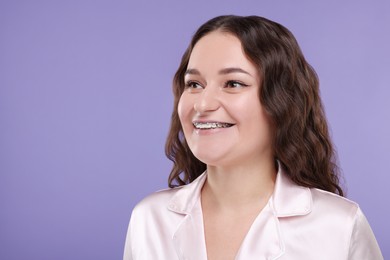 Smiling woman with dental braces on violet background, space for text