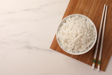 Bowl with delicious rice and chopsticks on white marble table, top view. Space for text