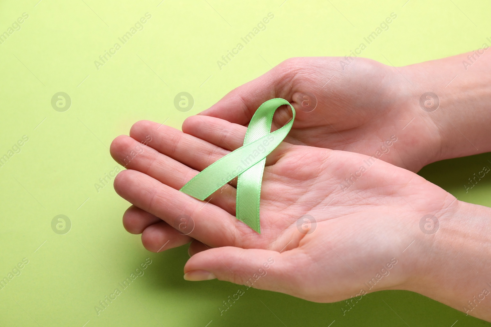 Photo of World Mental Health Day. Woman holding green ribbon on color background, closeup