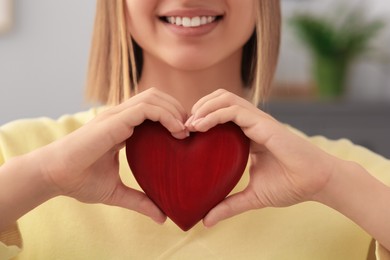 Young woman holding red heart indoors, closeup. Volunteer concept