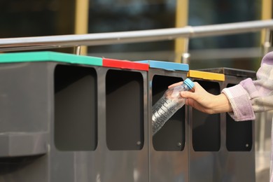 Photo of Woman throwing plastic bottle into sorting bin outdoors, closeup