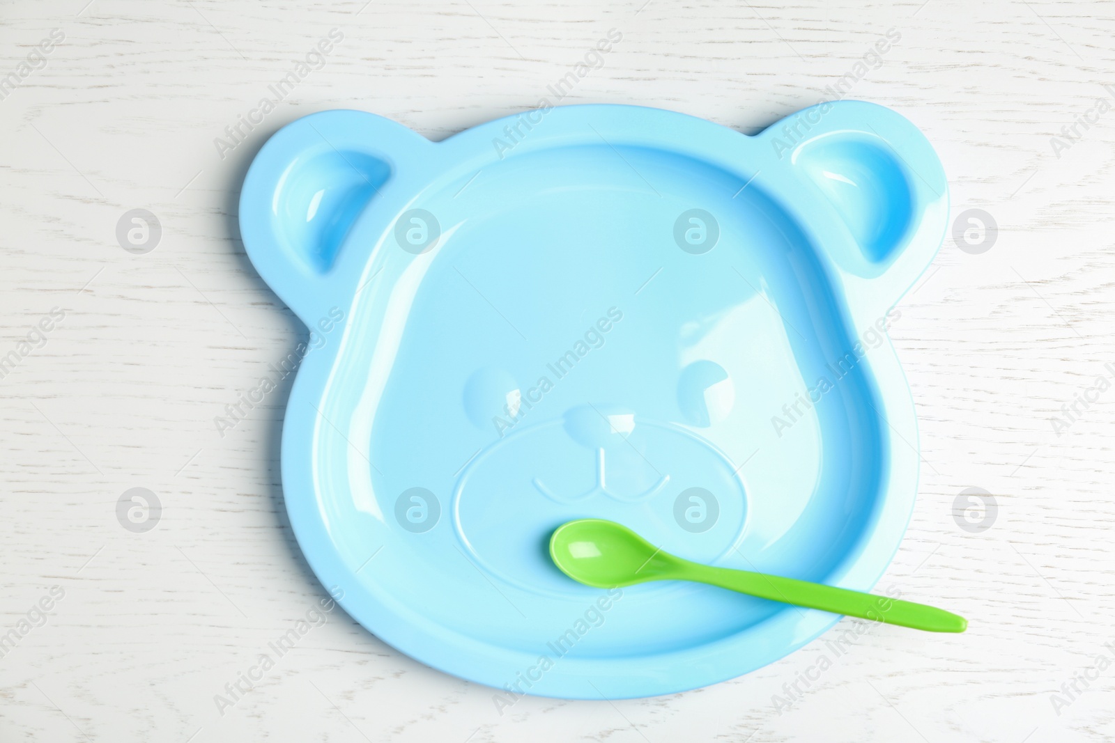 Photo of Cute animal shaped plate and spoon on white wooden table, top view. Serving baby food
