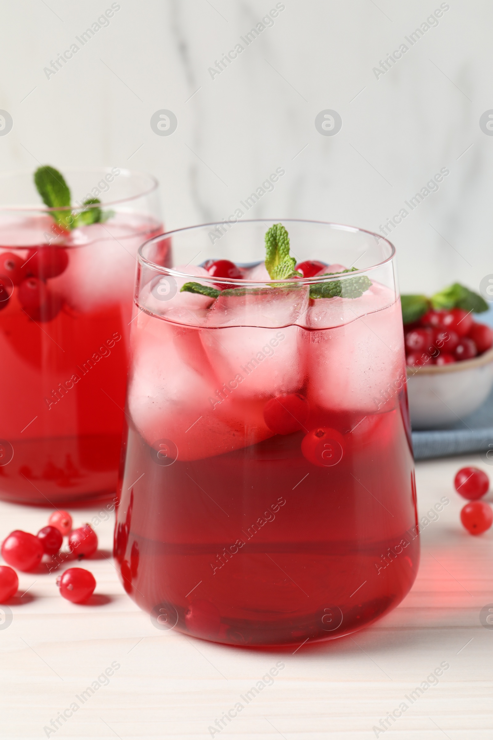 Photo of Tasty cranberry juice with ice cubes in glasses and fresh berries on white wooden table, closeup