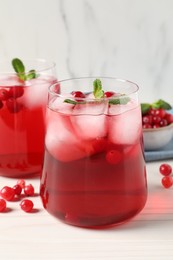 Photo of Tasty cranberry juice with ice cubes in glasses and fresh berries on white wooden table, closeup