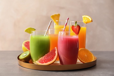 Photo of Tray with glasses of different juices and fresh fruits on table