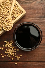 Photo of Soy sauce in bowl and soybeans on wooden table, flat lay