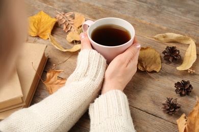 Woman with cup of hot drink at wooden table, closeup. Cozy autumn atmosphere