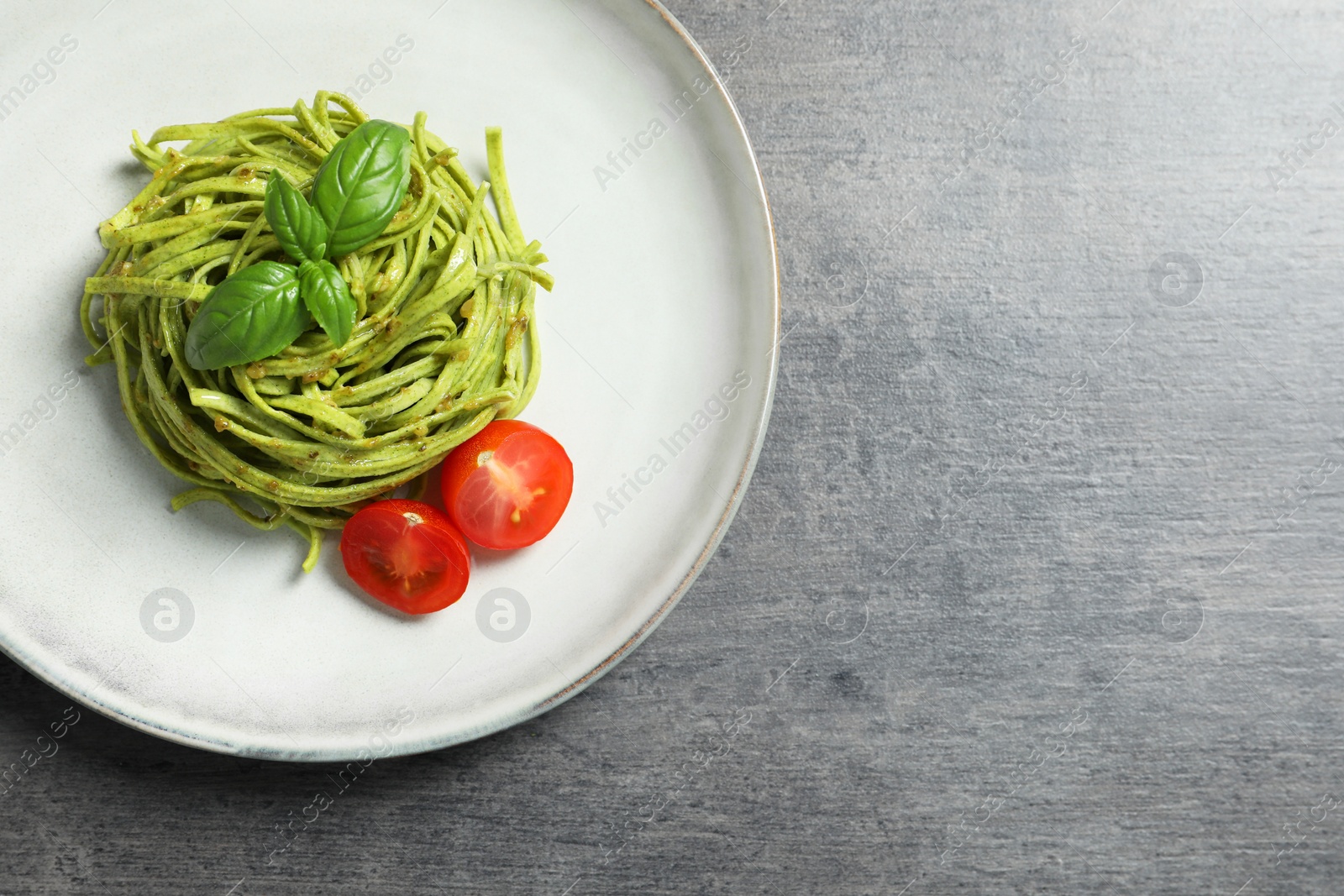 Photo of Tasty tagliatelle with spinach and tomatoes served on grey table, top view and space for text. Exquisite presentation of pasta dish