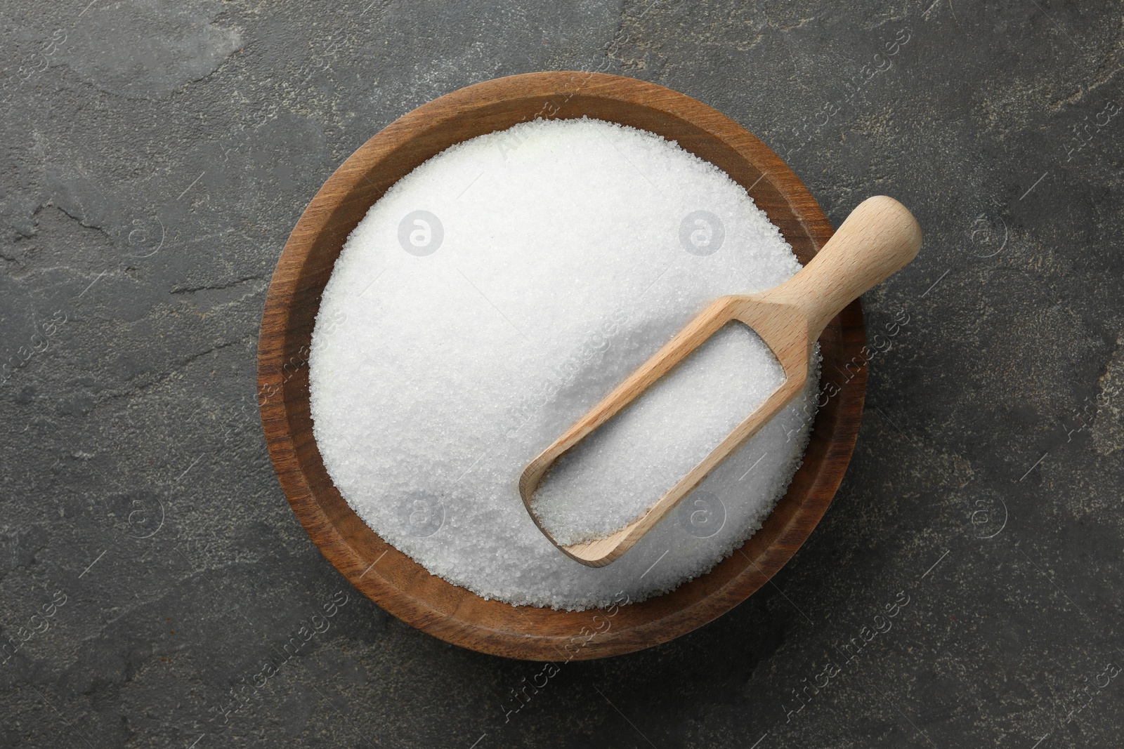 Photo of Granulated sugar in bowl and scoop on grey textured table, top view