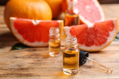 Bottles of essential oil, pipette and grapefruits on wooden table, space for text