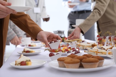 Photo of People near table with different delicious snacks during coffee break, closeup