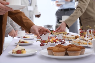 People near table with different delicious snacks during coffee break, closeup