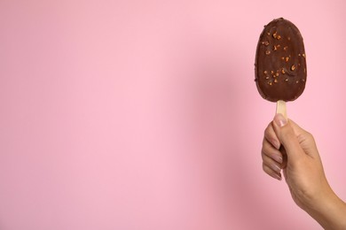 Photo of Woman holding ice cream glazed in chocolate on pink background, closeup. Space for text
