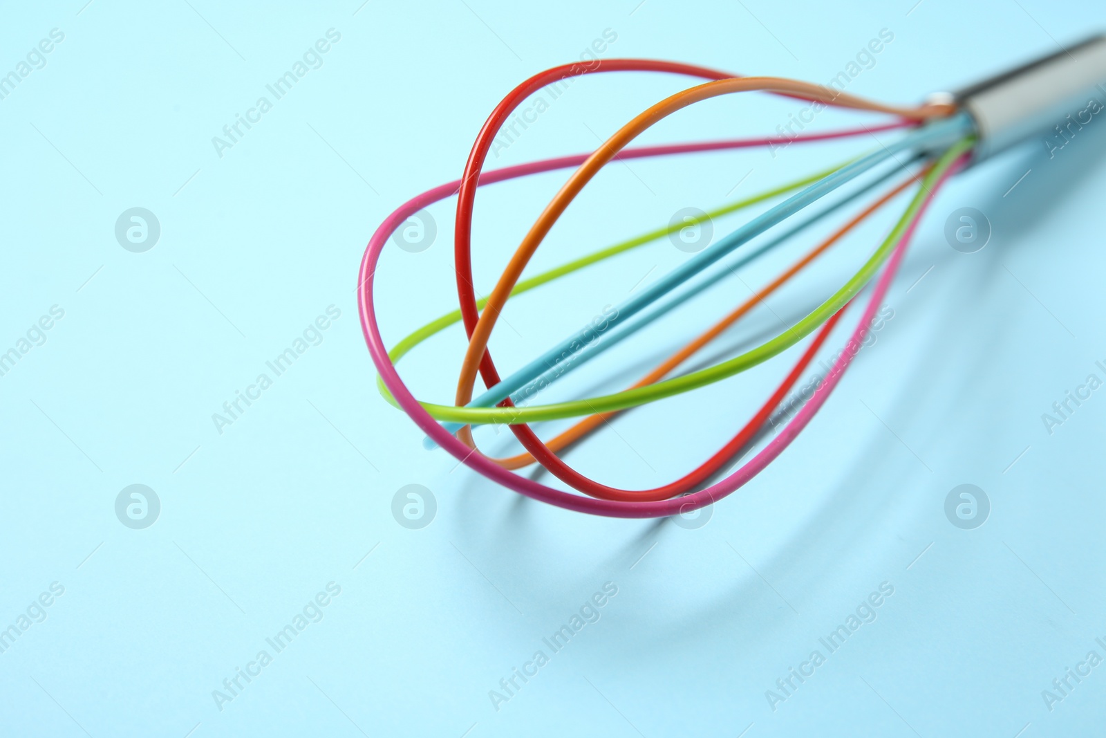 Photo of One whisk on light blue background, closeup. Space for text