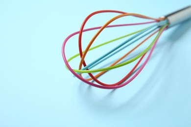 Photo of One whisk on light blue background, closeup. Space for text