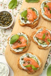 Photo of Tasty canapes with salmon, capers, cucumber and sauce on table, top view