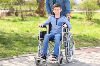 Preteen boy in wheelchair with his father at park on sunny day