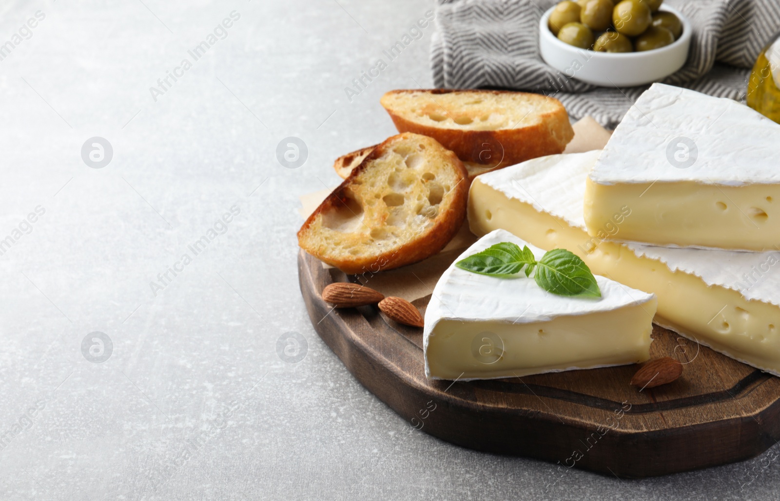 Photo of Tasty brie cheese with basil, bread and almonds on grey table, space for text