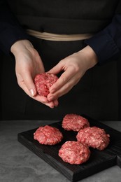 Photo of Woman making meatball from ground meat at grey table, closeup