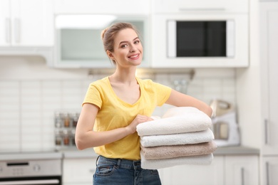 Woman holding folded clean towels in kitchen. Laundry day