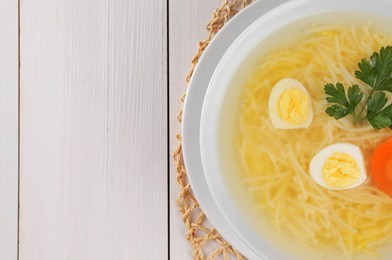 Photo of Tasty soup with noodles, egg, carrot and parsley in bowl on white wooden table, top view. Space for text