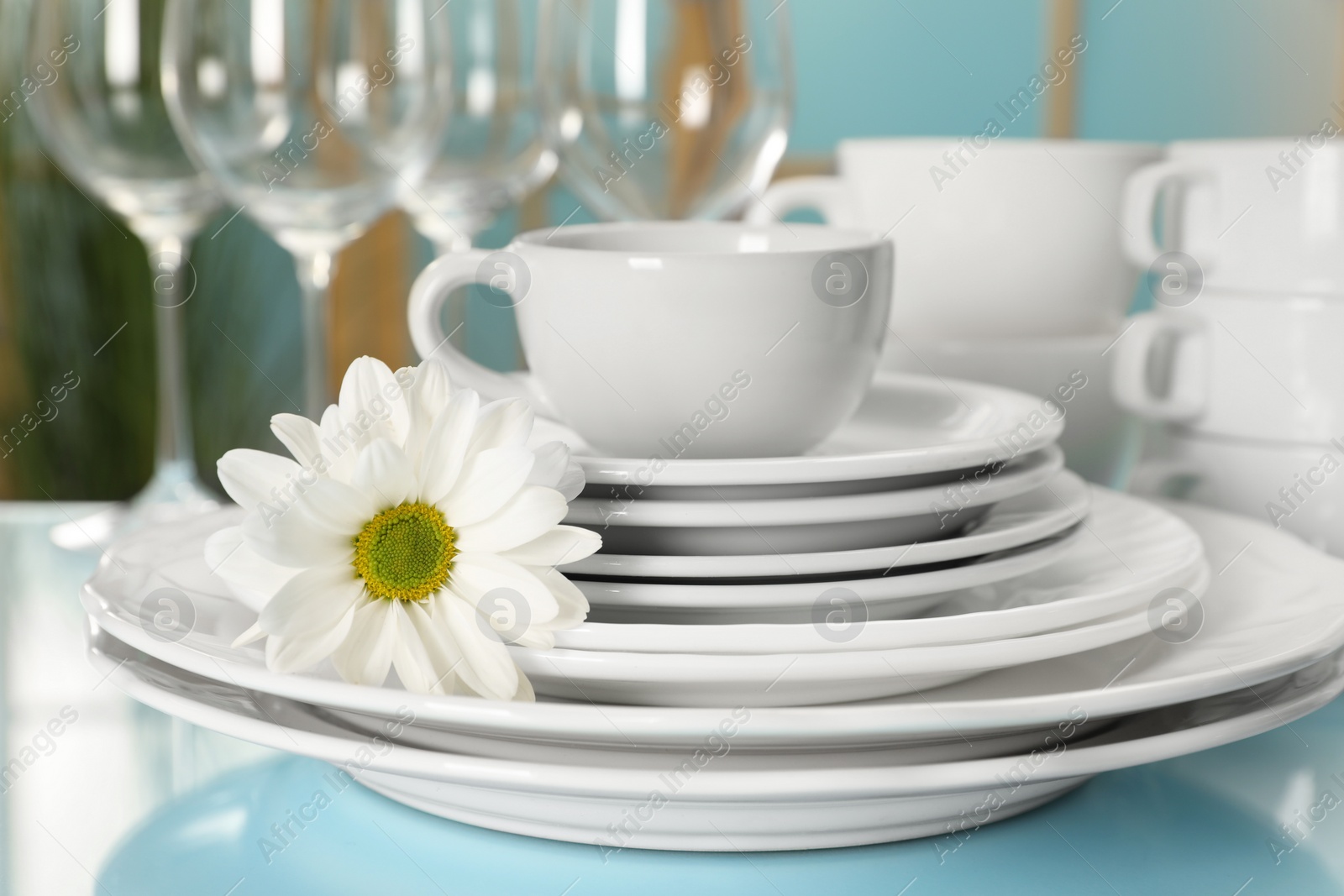 Photo of Set of clean dishware and flower on light blue table, closeup