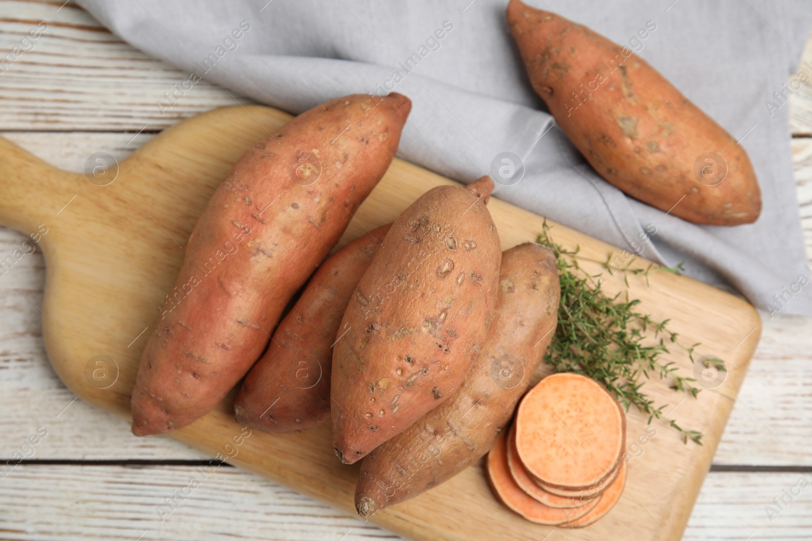 Photo of Wooden board with thyme and sweet potatoes on white table, flat lay