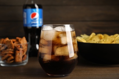 MYKOLAIV, UKRAINE - FEBRUARY 15, 2021: Glass of Pepsi and snacks on wooden table