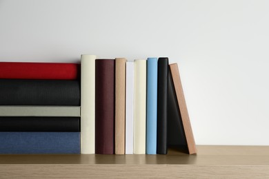 Many hardcover books on wooden table near white wall