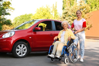 Photo of Senior woman in wheelchair with granddaughter near car outdoors