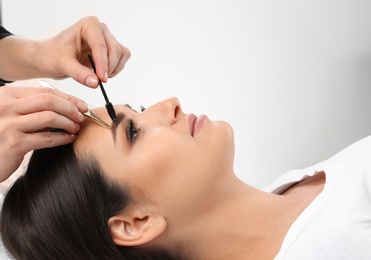 Photo of Young woman having professional eyebrow correction procedure in beauty salon