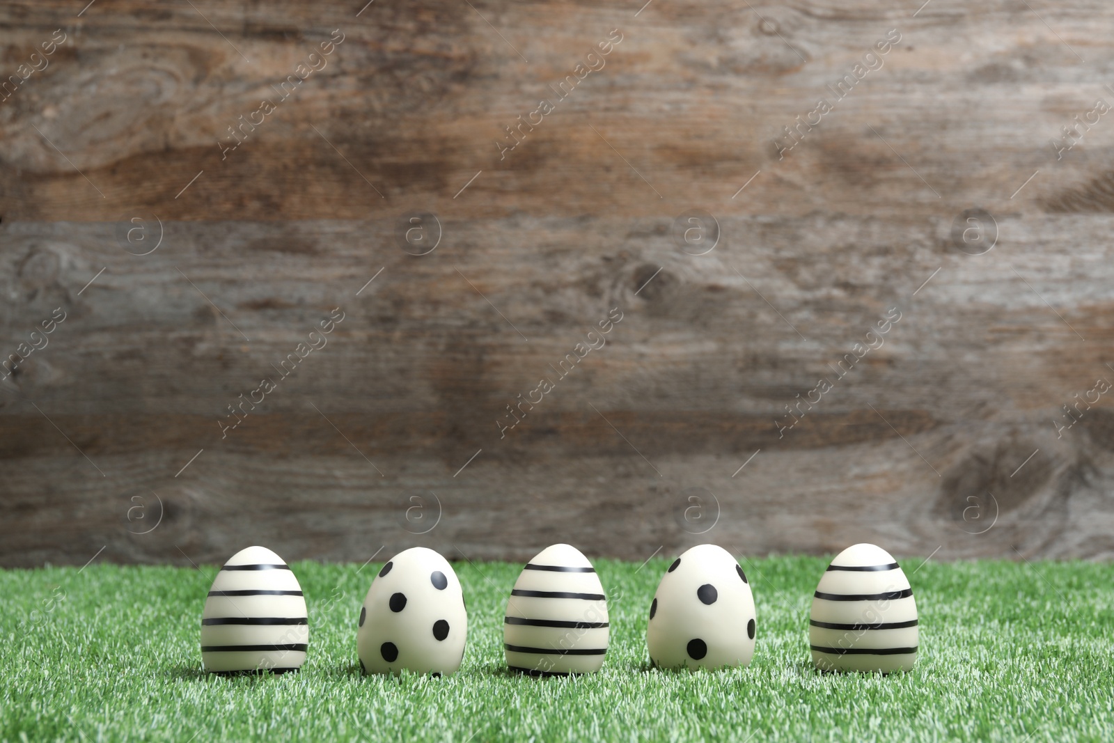 Photo of Line of traditional Easter eggs decorated with black paint on green lawn against wooden background, space for text