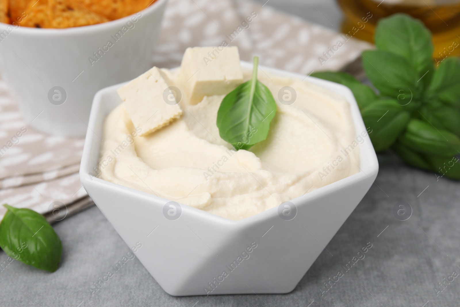 Photo of Delicious tofu sauce and basil leaves on grey table, closeup