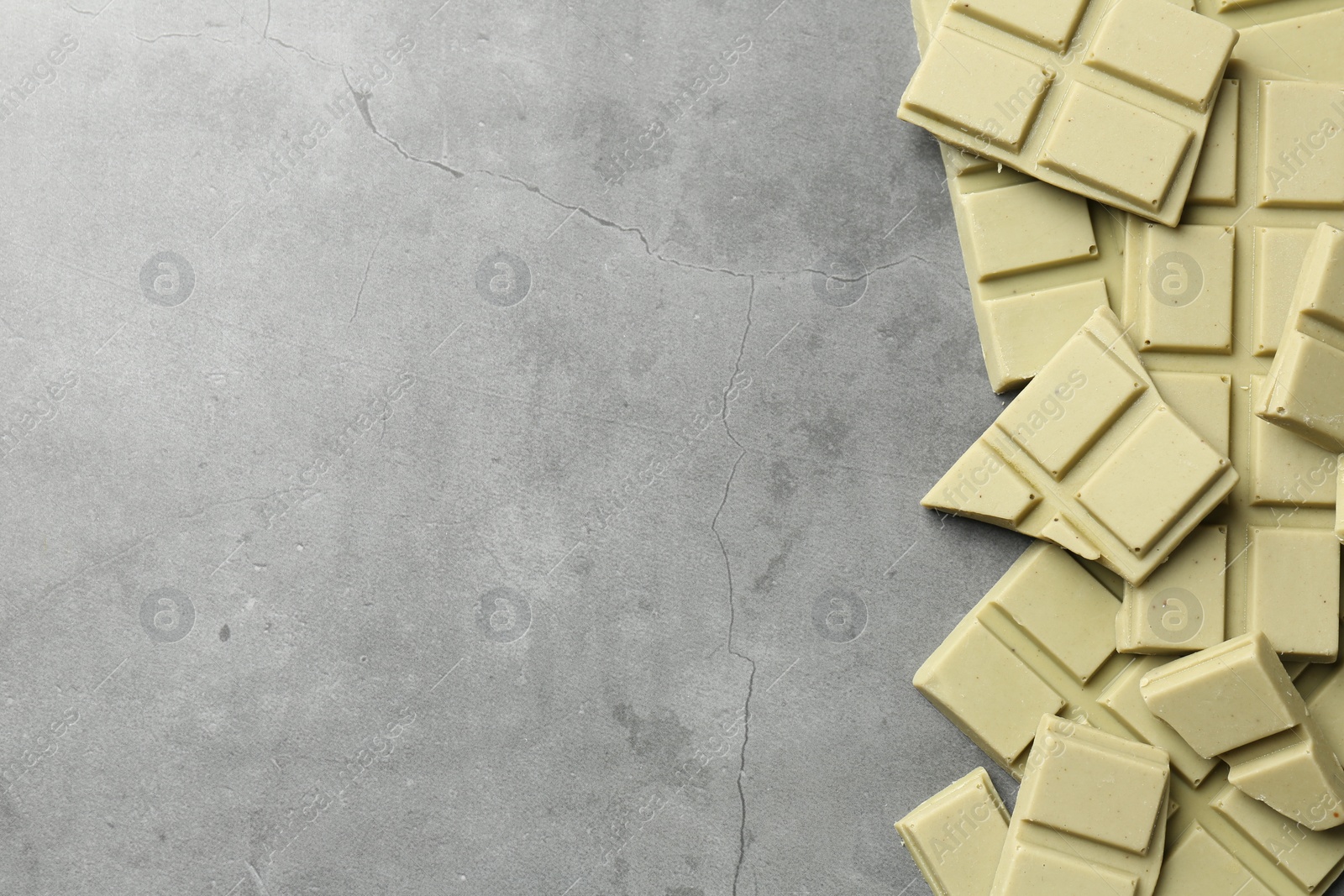 Photo of Pieces of tasty matcha chocolate bars on grey textured table, top view. Space for text