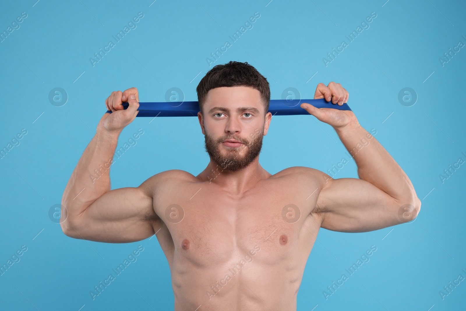 Photo of Young man exercising with elastic resistance band on light blue background