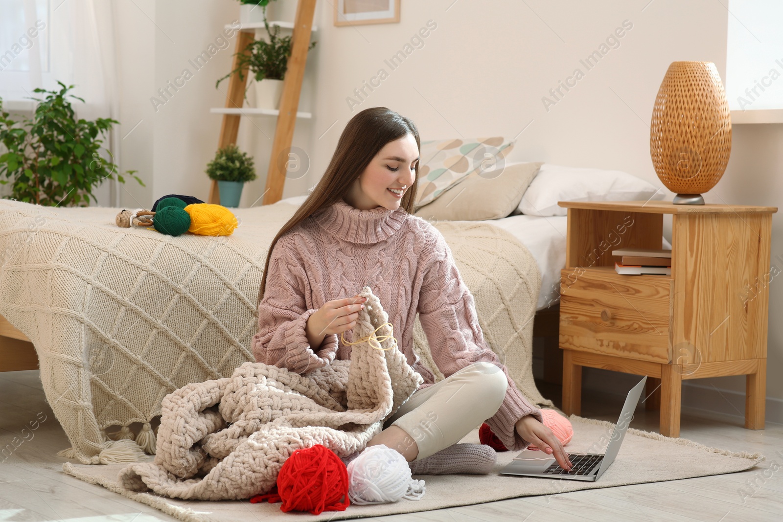 Photo of Young woman learning to knit with online course at home. Handicraft hobby