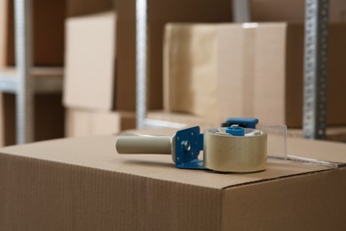 Photo of Adhesive tape dispenser on cardboard box indoors. Space for text